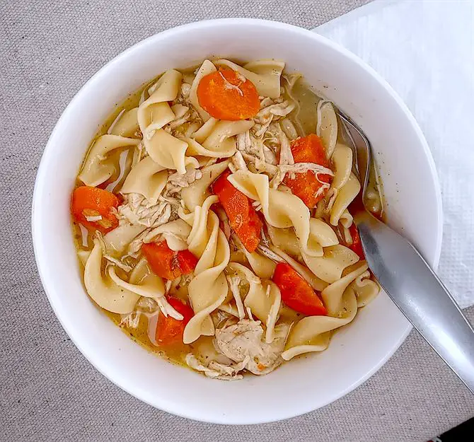 Chicken noodle soup in white bowl with a spoon
