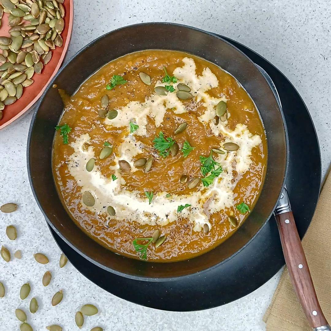 low sodium pumpkin soup in a black bowl with toasted pumpkin sees and cream drizzle top view featured image-(1)