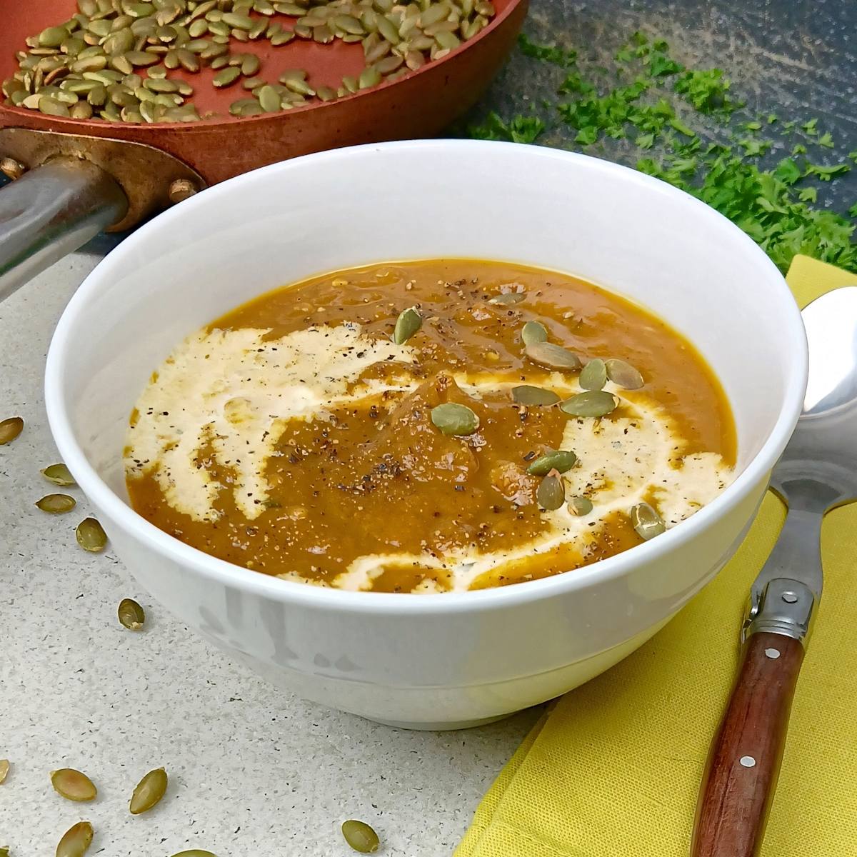 low sodium pumpkin soup in white bowl with cream drizzle pumpkin nuts angle view