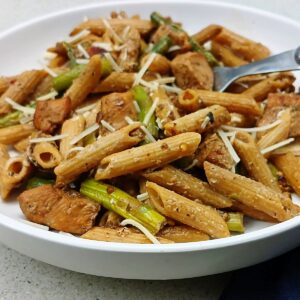 Close up of low sodium chicken pasta with asparagus in a low white bowl with fork.