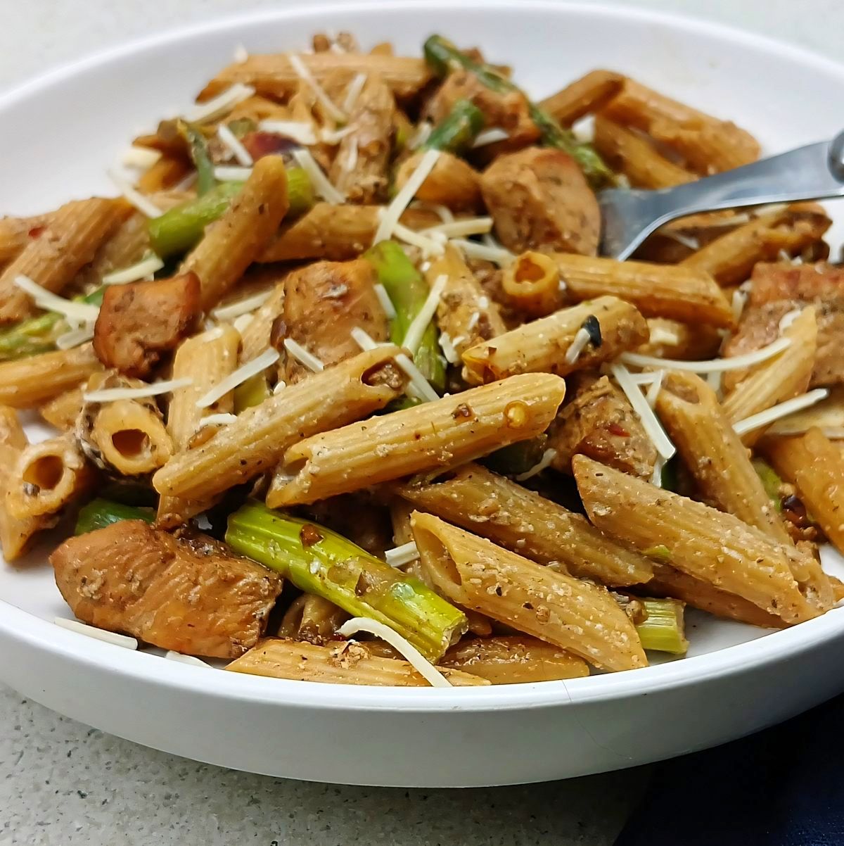 Close up of low sodium chicken pasta with asparagus in a low white bowl with fork.