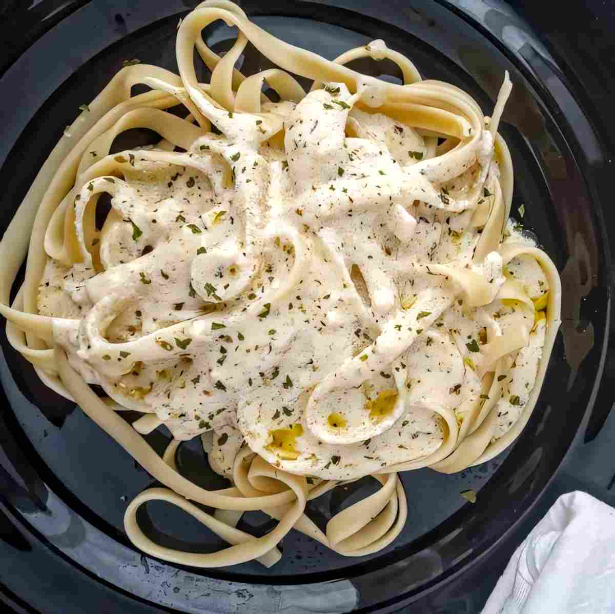 Alfredo sauce over fettuccine noodles on a black plate.