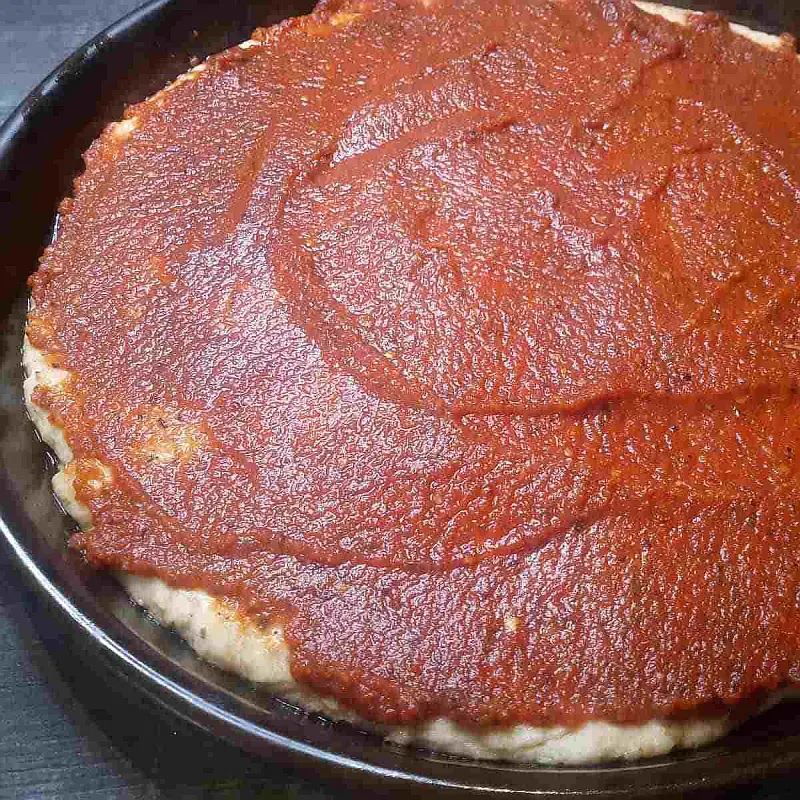 Pizza sauce spread over dough in pizza pan.