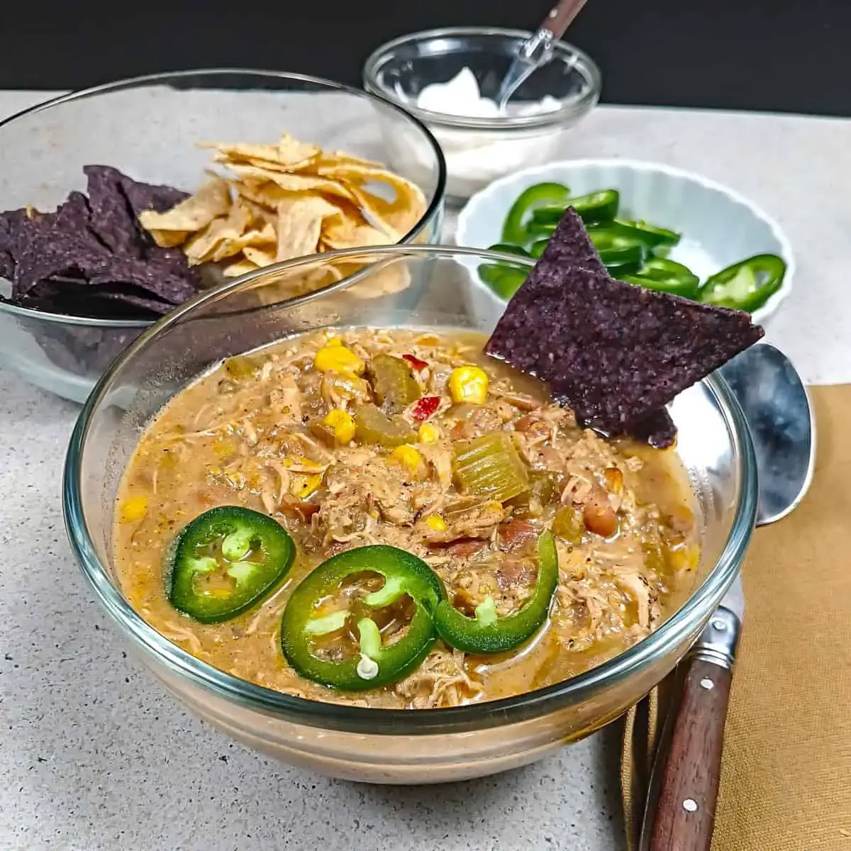 Chili in clear glass bowl with sliced jalapenos and blue tortilla chips.