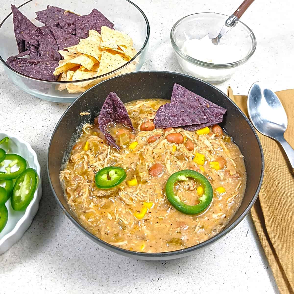 Chili in a black bowl with sour cream tortilla chips and jalapeno slices accoutrements bowls.