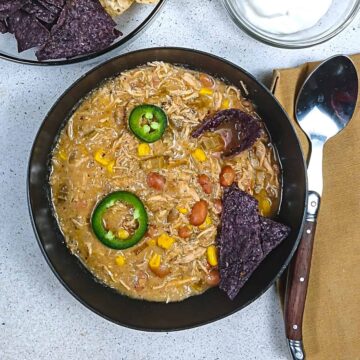 Close up of chili in a black ball with jalapeno slices and tortilla chips.