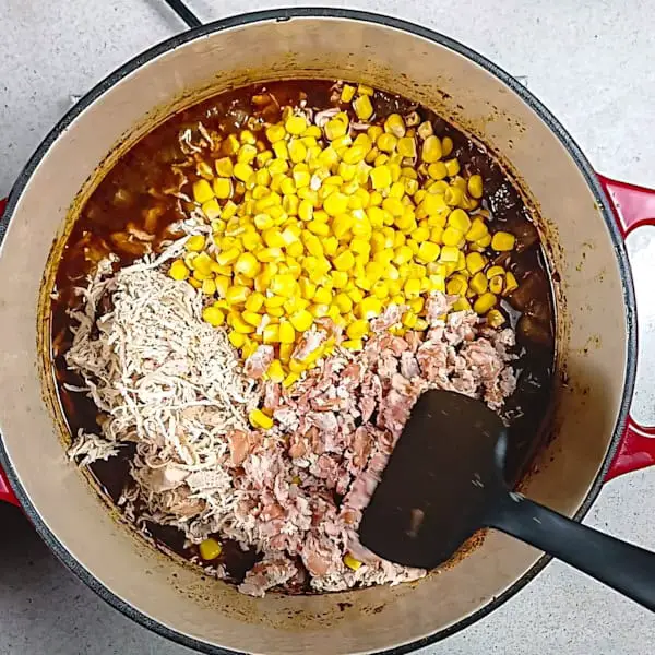 Adding shredded chicken, corn, and mashed beans to the pot.