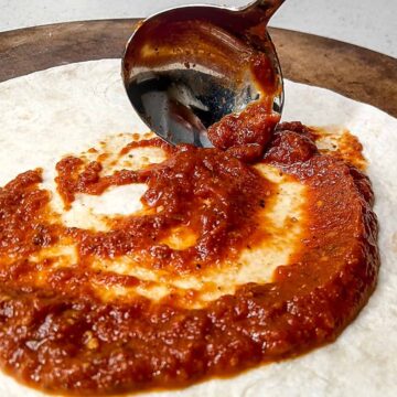 Pizza sauce being ladled on dough.